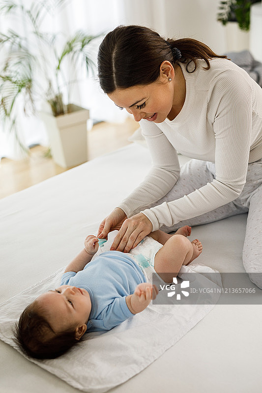 年轻妈妈在家为她的小男婴换尿布图片素材