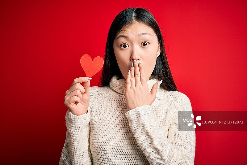 年轻亚洲女人拿着红色爱心纸片，捂嘴震惊，感到羞愧和害怕图片素材