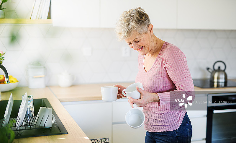 一位妇女在家里的厨房里，卸载洗碗机。图片素材