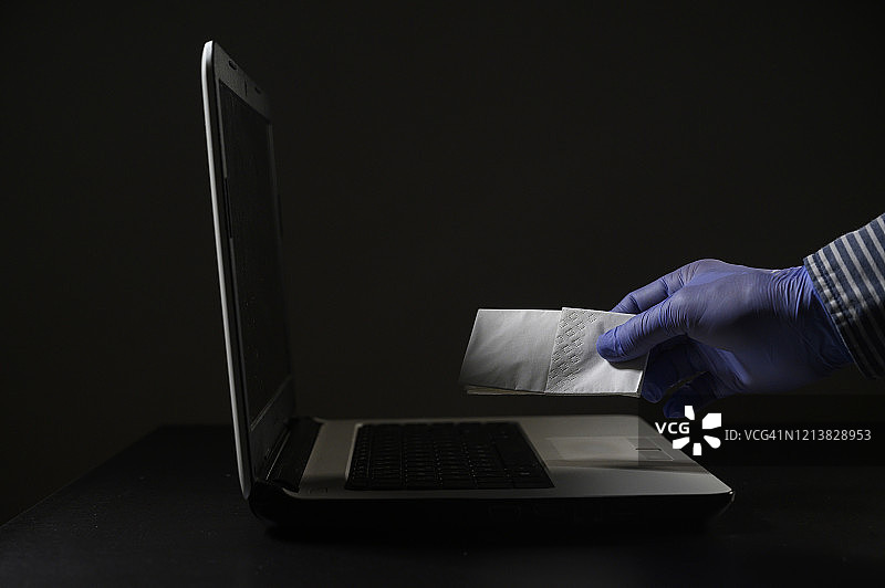 戴着防护手套清洁笔记本电脑，以防止接触冠状病毒等病毒的手图片素材