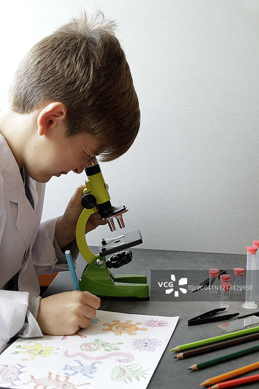 在显微镜下寻找病毒并绘制它们的男孩图片素材