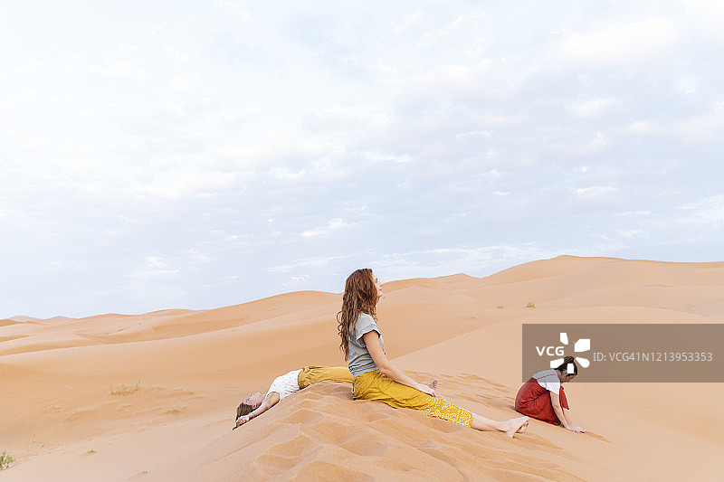 三名年轻女子在摩洛哥梅尔祖卡撒哈拉沙漠的沙丘中休息图片素材