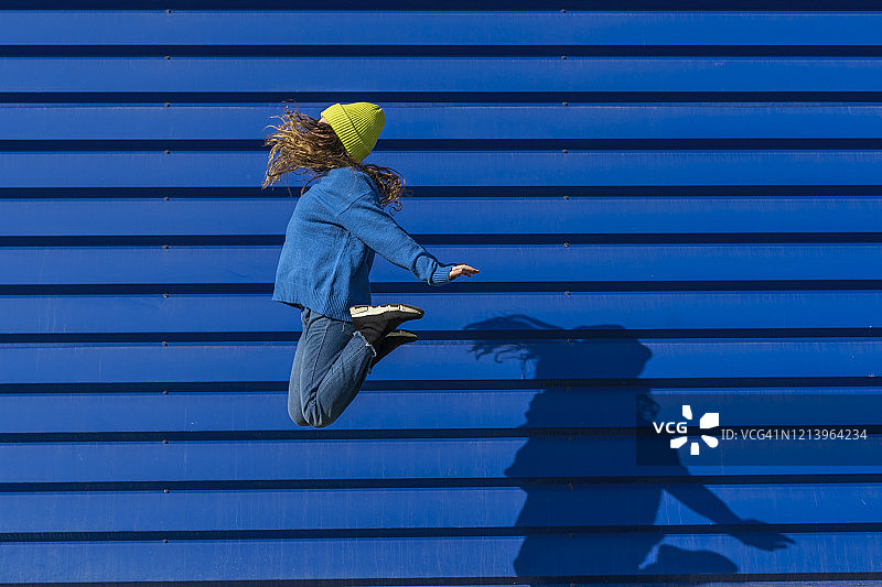 少女在蓝色背景前跳跃图片素材