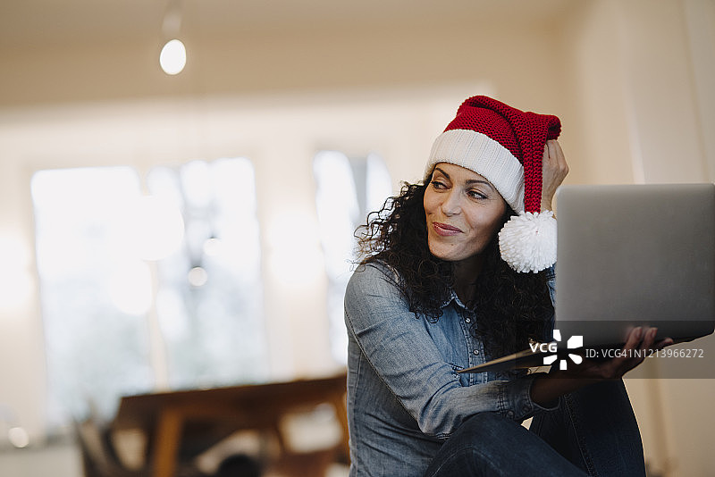 戴圣诞帽用笔记本电脑在网上寻找礼物的女人图片素材