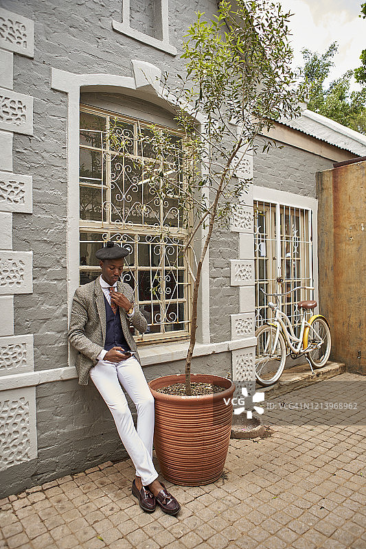 戴着贝雷帽倚靠在墙上的时尚年轻商人图片素材