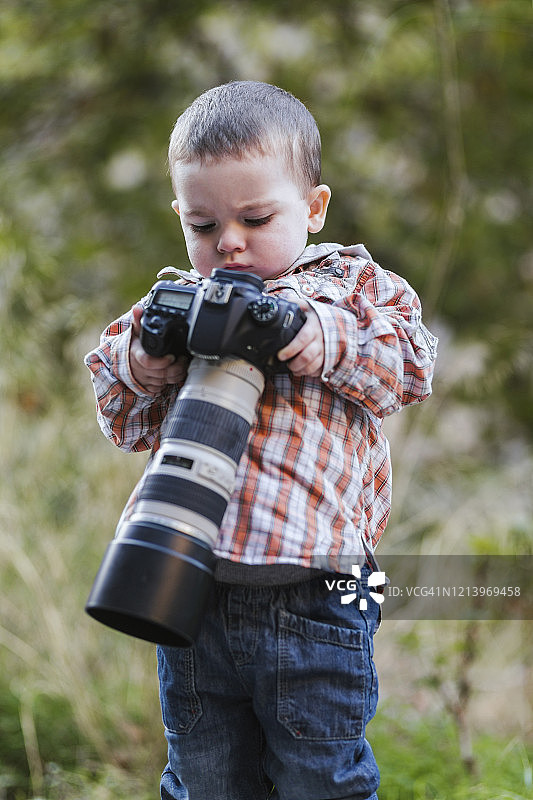 在户外看着带大镜头的数码单反相机的幼儿画像图片素材
