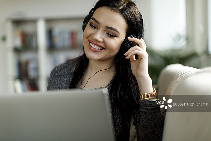 年轻女人戴着耳机在家使用笔记本电脑图片素材