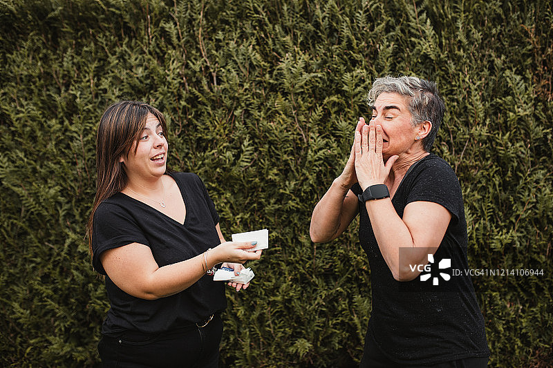 两位年轻女性，一位因春季过敏打喷嚏，另一位递给她纸巾图片素材