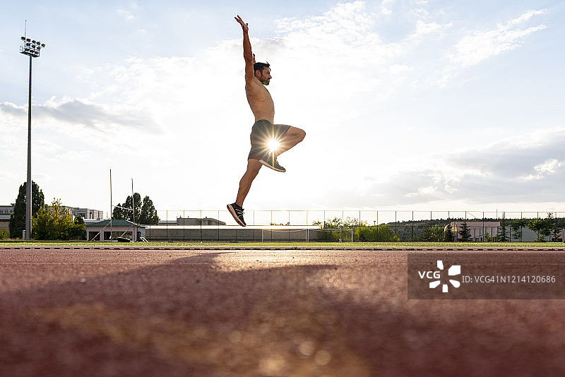 年轻男人在日出时于体育场的跑道上慢跑和跑步。田径运动中的跳远图片素材