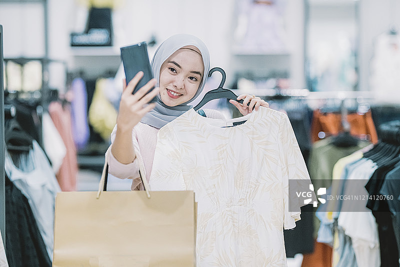 马来西亚穆斯林妇女在斋月期间购物，购买衣服并自拍和视频通话图片素材
