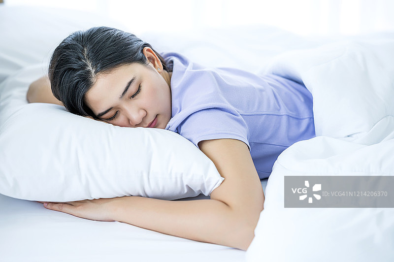 年轻亚裔女性在床上睡觉，拥抱柔软的白色枕头，舒适休闲概念图片素材