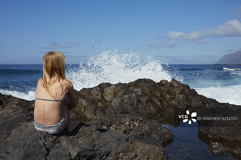 女孩坐在海滩的熔岩石上观看大海图片素材