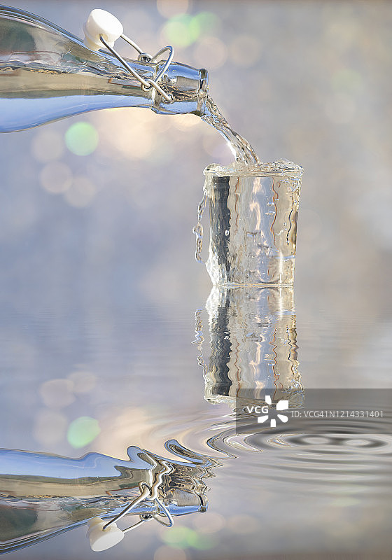 阳光照射下，玻璃水瓶向玻璃杯中注水，水中倒影图片素材