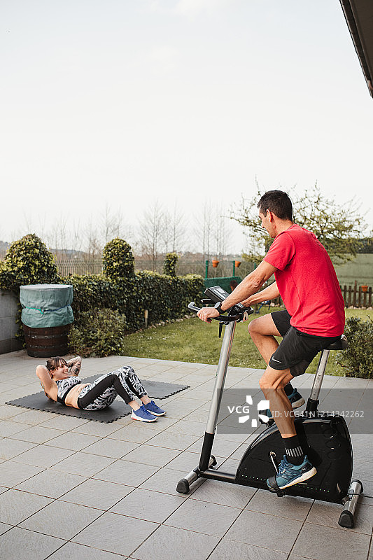 中年男人和年轻女人在日落时分在他家的露台上穿着运动服锻炼图片素材