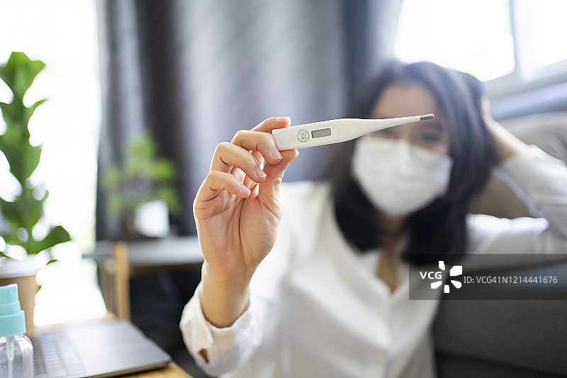 亚洲女性在家中使用体温计检测体温，检查是否发烧或感染新冠病毒，居家隔离14天图片素材