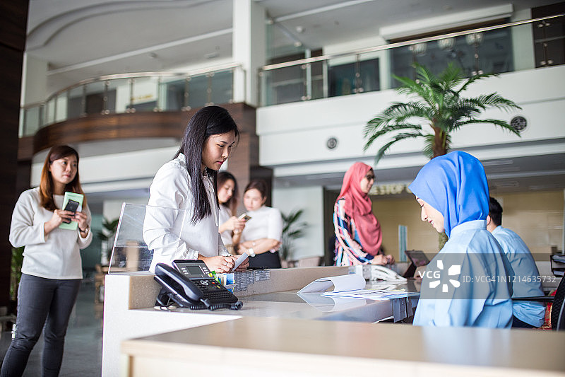 医务人员在医院接待处协助女患者，提供诊所帮助和护理。患者家属在接待处排队等候图片素材