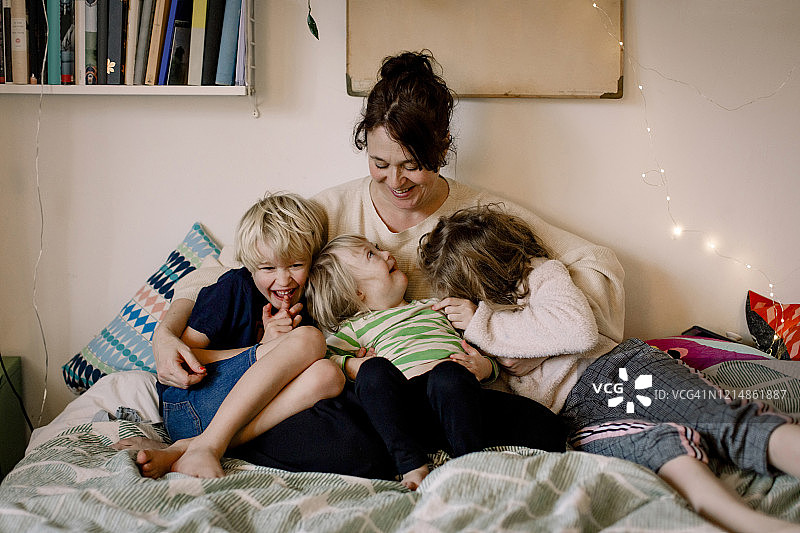 微笑的残疾女孩在卧室里和兄弟姐妹坐在一起，看着妈妈图片素材