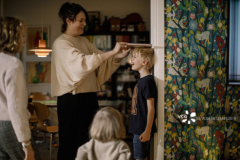 母亲用书本在墙上测量微笑儿子的身高图片素材