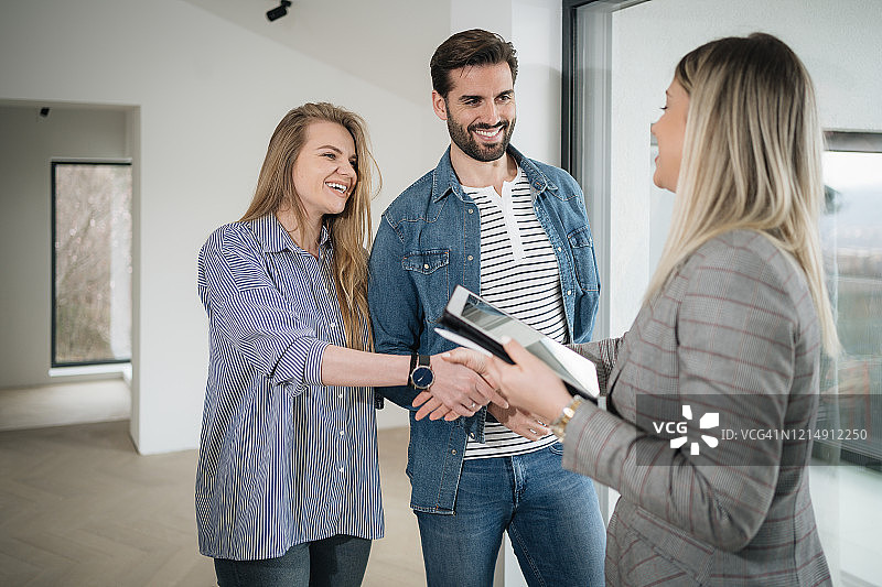 房产经纪人与年轻夫妇握手，成功售房图片素材