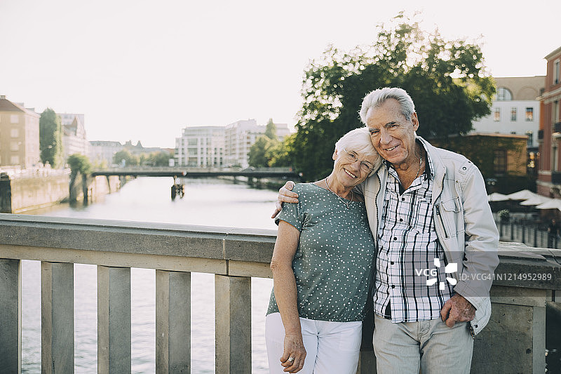城市中靠在栏杆旁微笑的年长夫妇肩并肩站立肖像图片素材