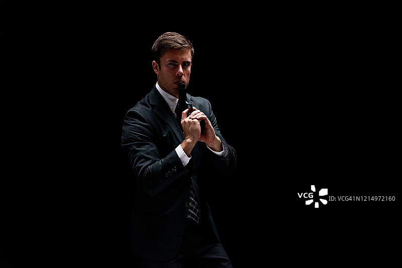 穿商务装的年轻白人商务人士在黑色背景前持武器用枪图片素材