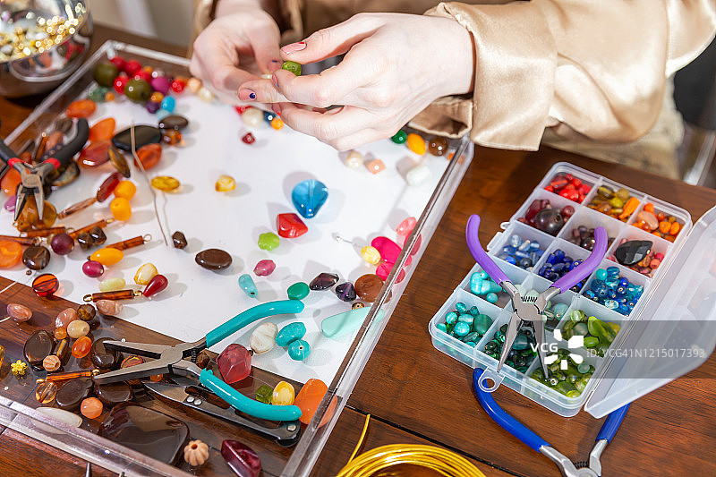 女模特在工作台上使用珠子、钳子和其他工具制作珠宝图片素材