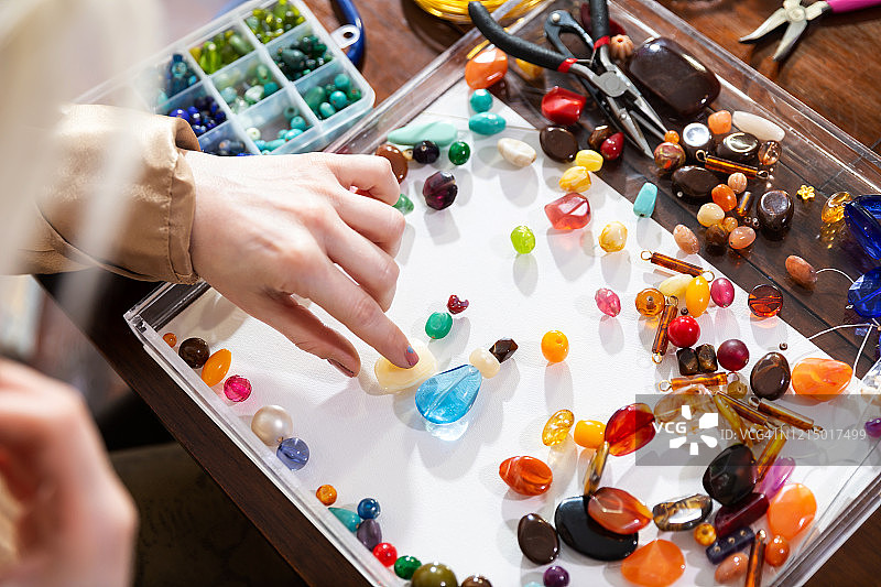 女模特在工作台上使用珠子、钳子和其他工具制作珠宝图片素材