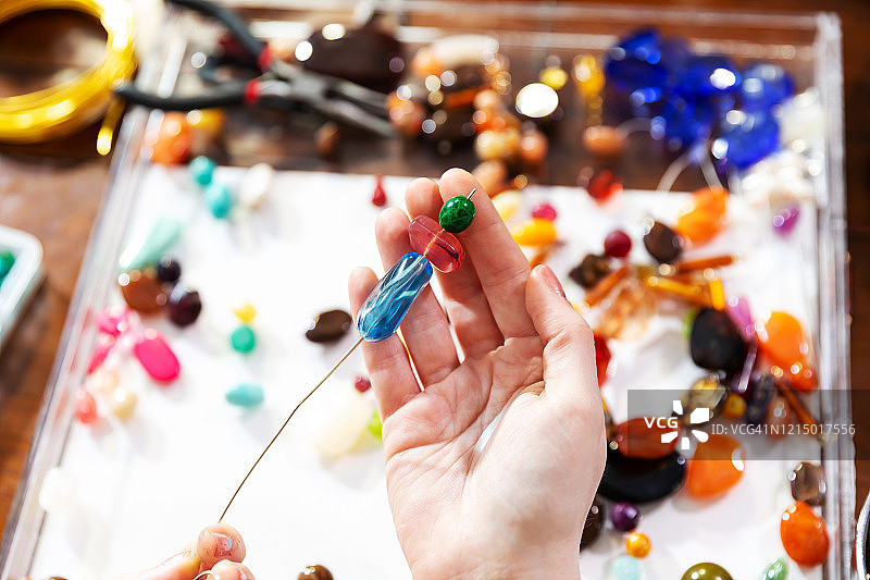 女模特在工作台上使用珠子、钳子和其他工具制作珠宝图片素材