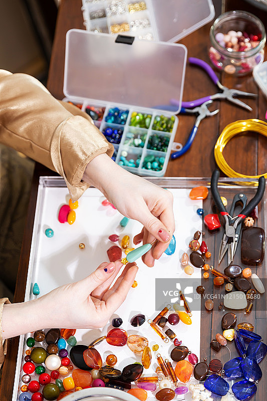 女模特在工作台上使用珠子、钳子和其他工具制作珠宝图片素材