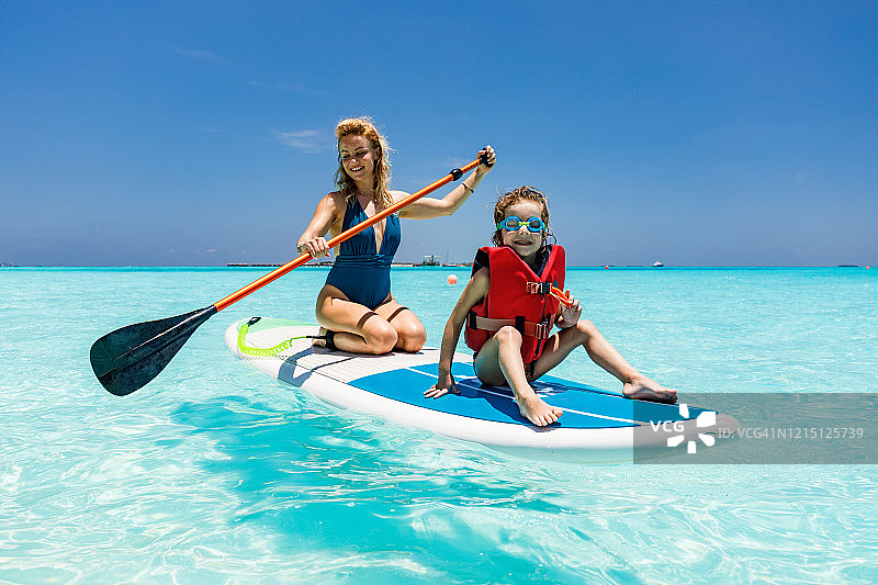 快乐的母亲和儿子在夏日的海上玩桨板图片素材