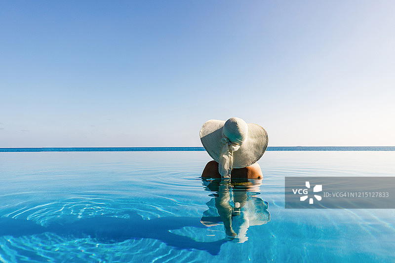 戴着遮阳帽在无边泳池里的女子背影图片素材