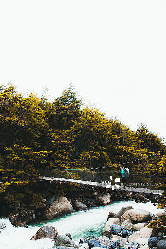 在智利巴塔哥尼亚山区，女背包客通过悬索桥过河图片素材