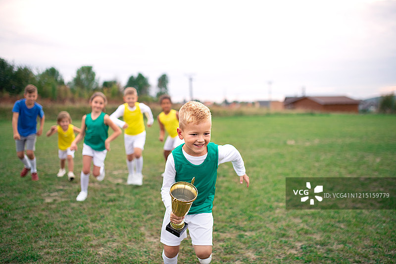 一群快乐的孩子在足球场上跑步，手捧奖杯图片素材
