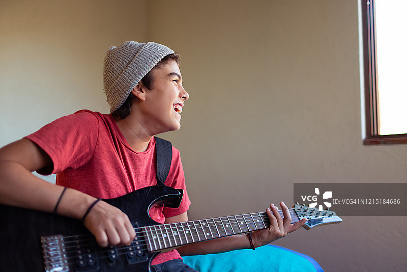 快乐地在房间里弹电吉他的拉丁裔青少年图片素材