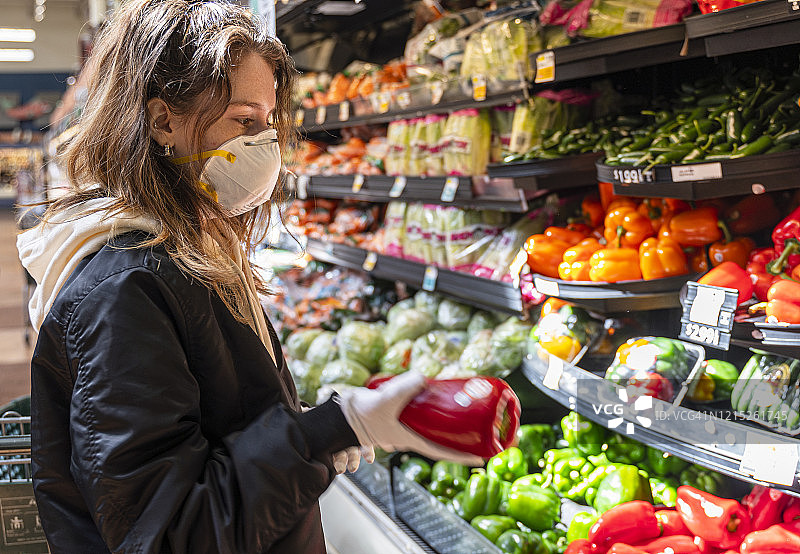 疫情期间购物：一位戴着防护口罩和手套的年轻女子在商店购买蔬菜图片素材