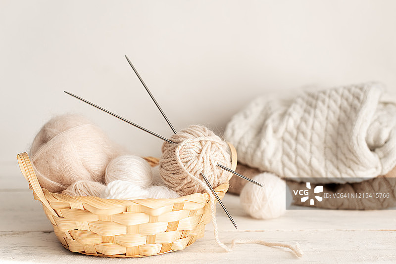 老式针织针、剪刀和纱线在木凳上的旧金属丝篮子里，柔焦静物照片图片素材