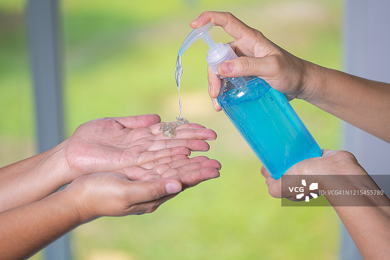 女性从酒精清洗泵瓶中获得酒精凝胶，人们使用酒精凝胶洗手以预防细菌和新冠病毒图片素材