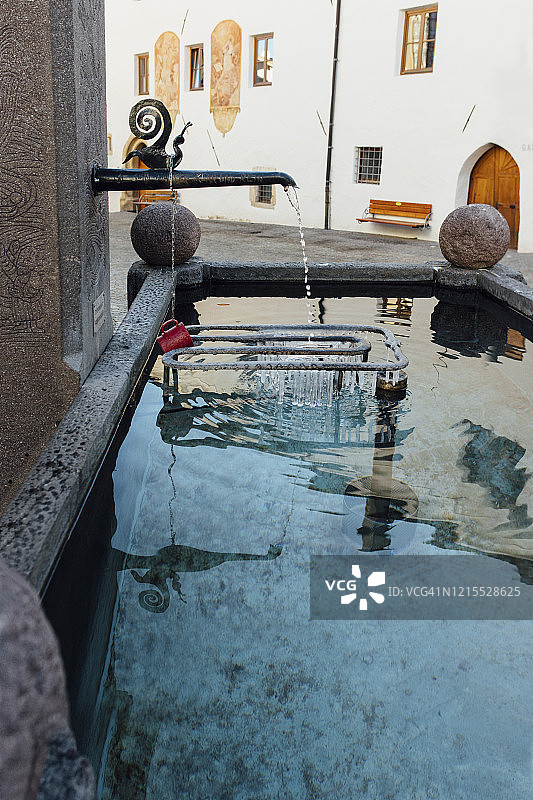 锻铁蜗牛装饰水龙头，倒映在带饮水杯的石制喷泉中图片素材