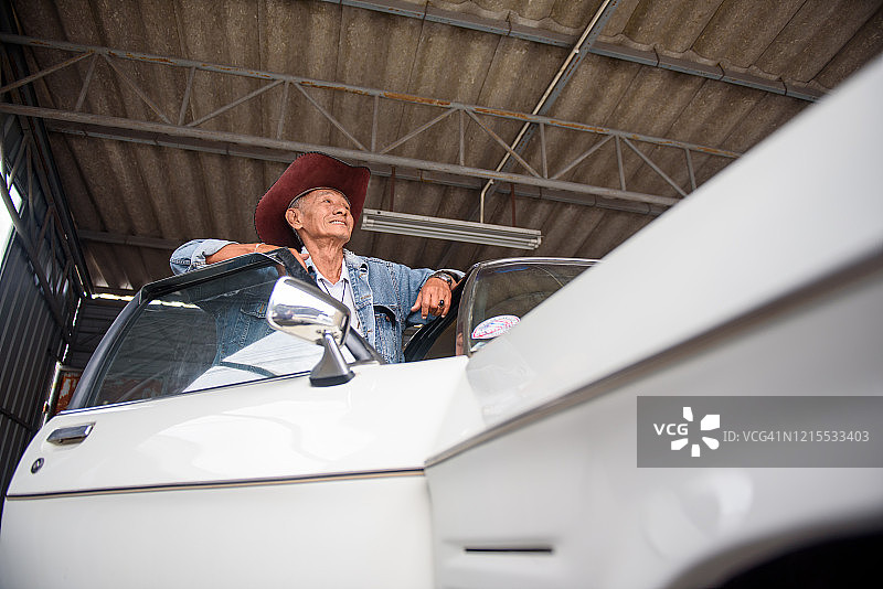 穿着复古牛仔夹克的亚洲老人在老爷车旁摆姿势图片素材