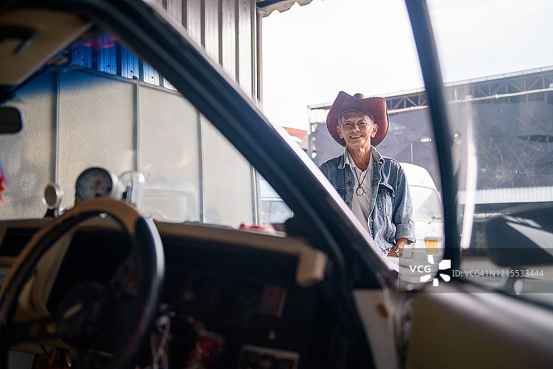 穿着复古牛仔夹克的亚洲老人在老爷车旁摆姿势图片素材