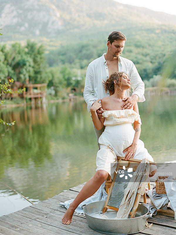 孕妇与男子身穿复古服装在河边金属盆中清洗亚麻布，环保洗衣概念图片素材