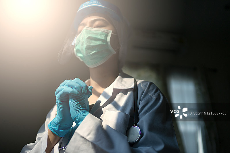 戴着防护面罩和个人防护装备的亚洲女医生祈祷停止新冠疫情图片素材