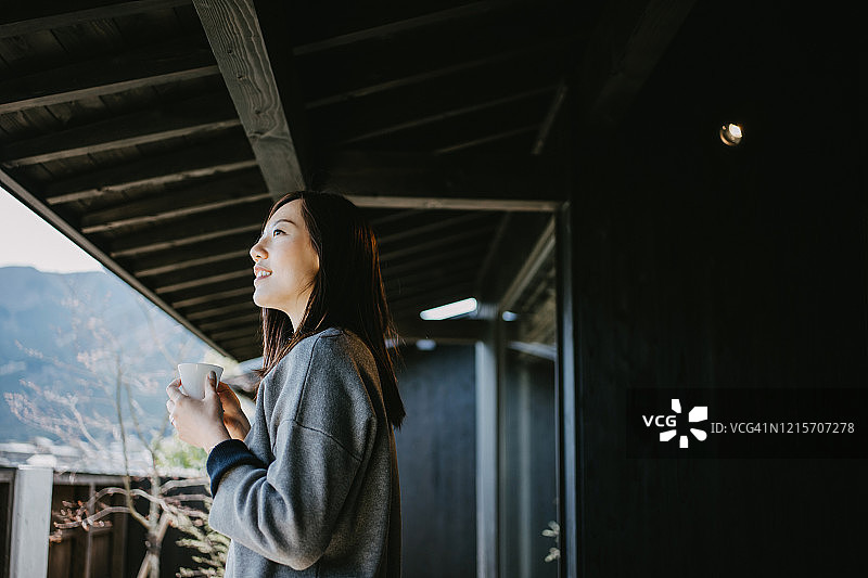 年轻亚洲女子在阳台上喝咖啡放松图片素材