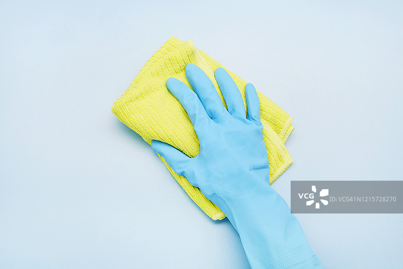 戴手套的手拿着黄色清洁抹布，蓝色背景图片素材