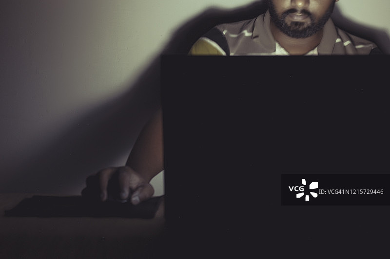 男子在黑暗房间使用笔记本电脑的肖像照图片素材