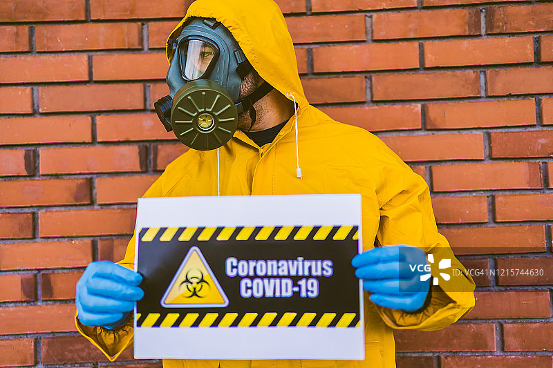 身穿防护服，手持带生物危害标志的冠状病毒标志的男人图片素材