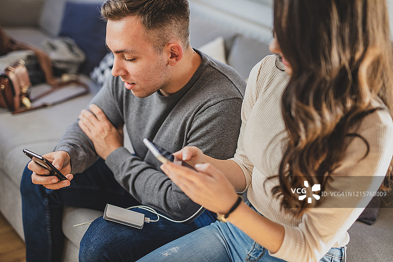 情侣在沙发上使用智能手机和充电宝图片素材