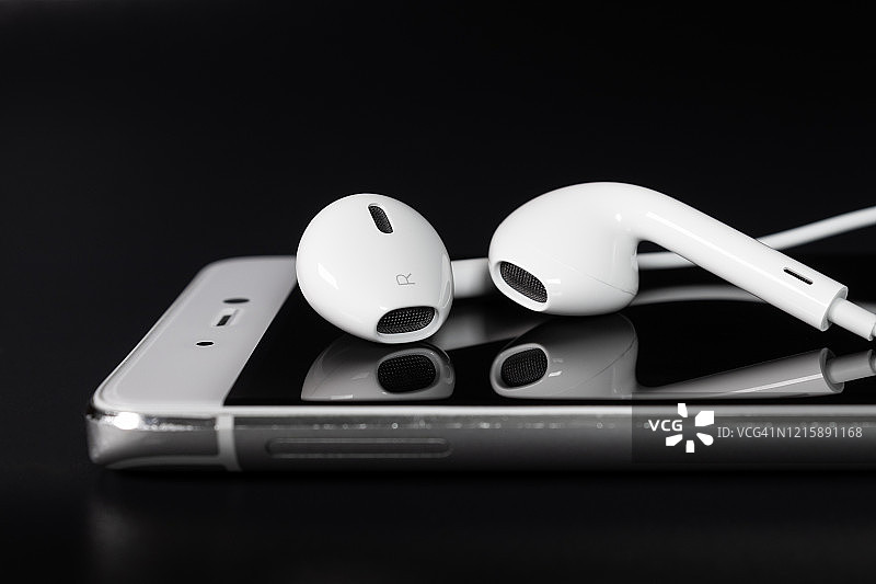 耳机放在手机屏幕上，背景为黑色图片素材