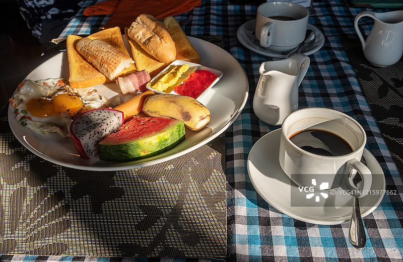 木桌上的欧式早餐套餐，包括面包、黄油、果酱、鸡蛋、肉类、水果和各种热饮图片素材