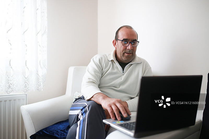 中年男人在家中客厅用笔记本电脑做研究，社交隔离图片素材